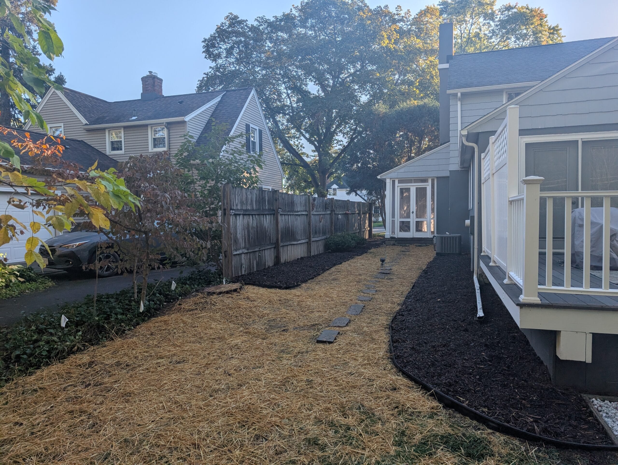 Newly reseeded yard covered in straw, surrounded by garden beds with fresh mulch, showcasing professional lawn seeding and renovation by EJ Lawn & Landscape in Brighton, NY