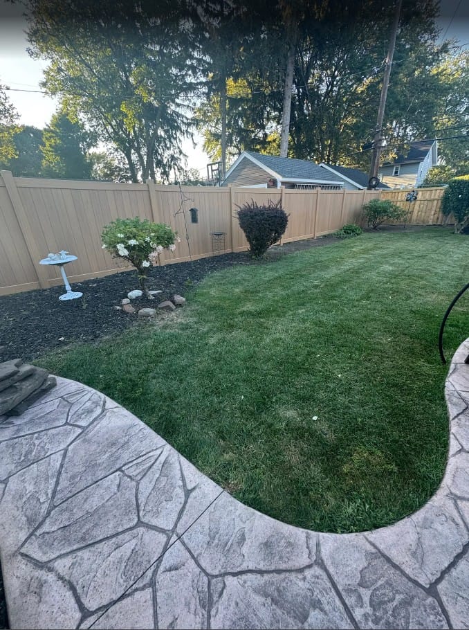 Freshly mowed backyard with surrounding garden, showcasing professional lawn care by EJ Lawn & Landscape in Irondequoit, NY