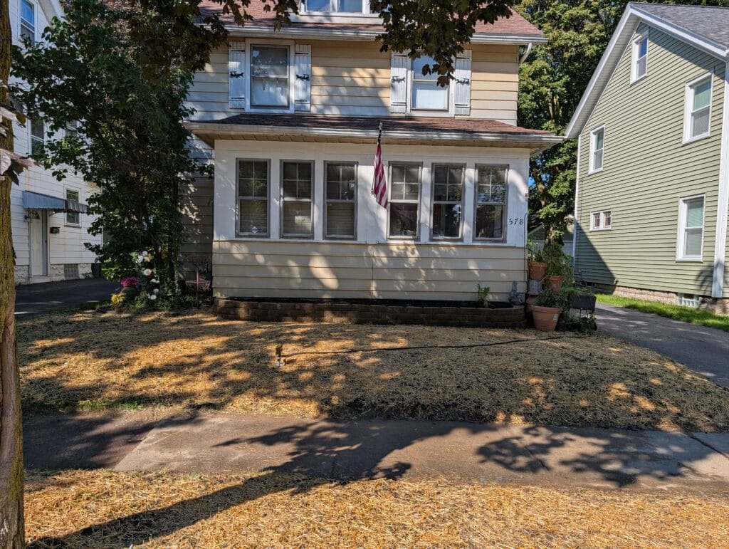 Completed stone retaining wall with newly seeded front yard covered in straw in Rochester NY