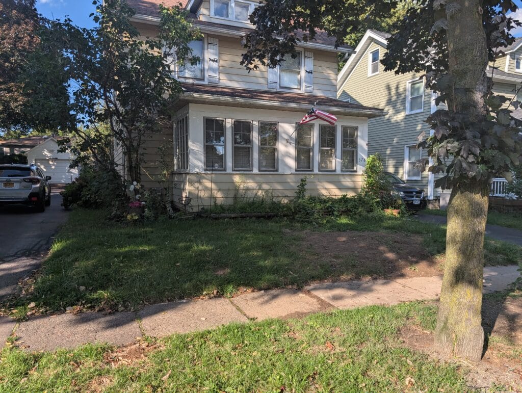 Large bare patch in front yard with overgrown garden and rotting timbers in Rochester NY
