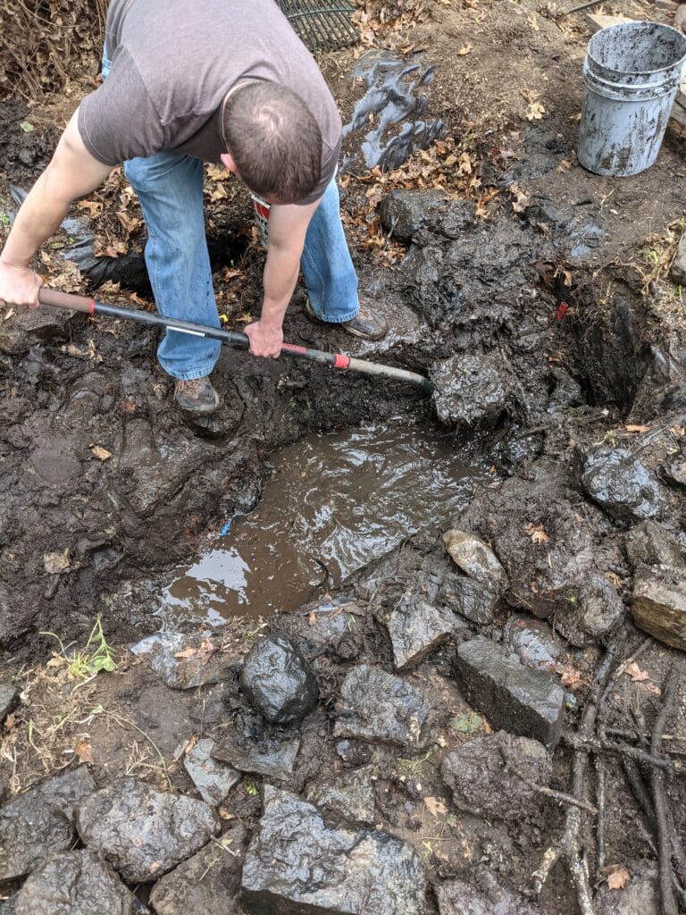Workers digging rocks out of an old pond in Irondequoit as part of pond removal and patio installation.