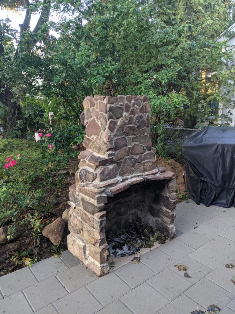 Completed stone fireplace in Irondequoit built with reclaimed pond rocks at the edge of a patio.