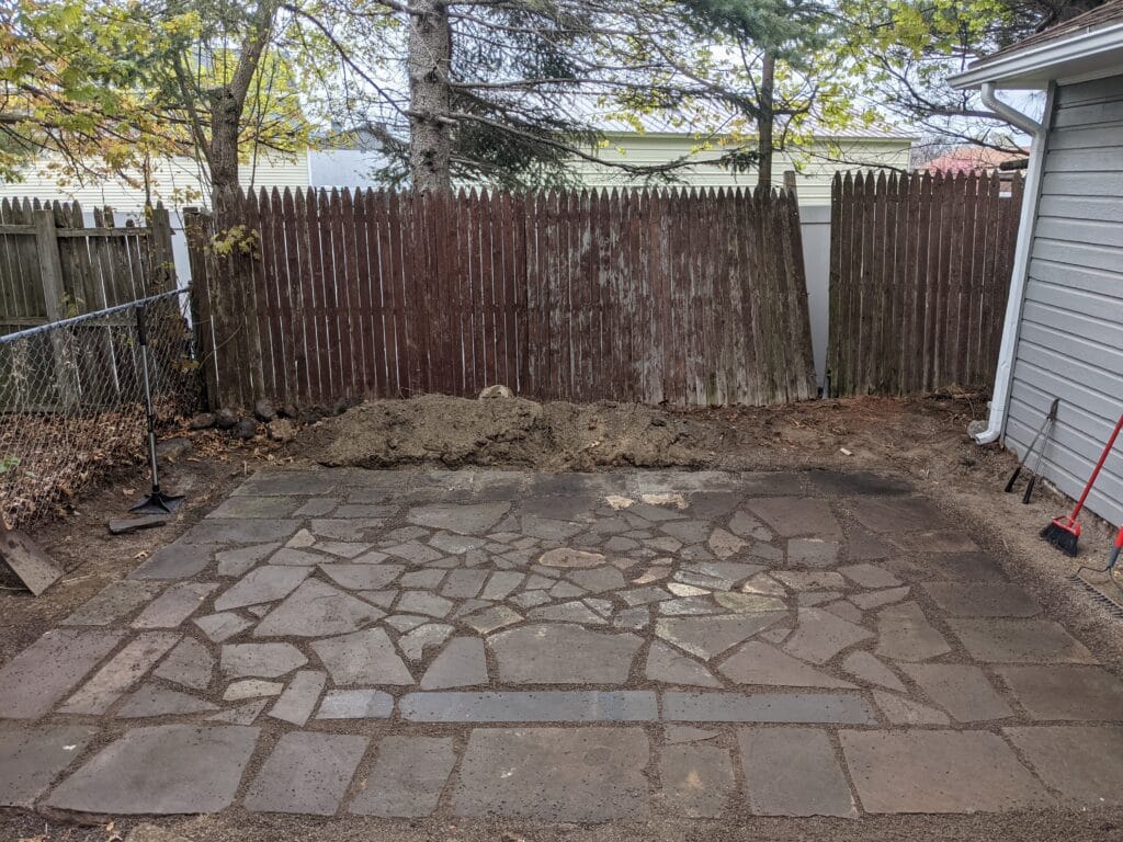 Completed natural stone patio in Irondequoit, NY, with hand-placed stones and paver base, creating a durable and elegant outdoor living area.