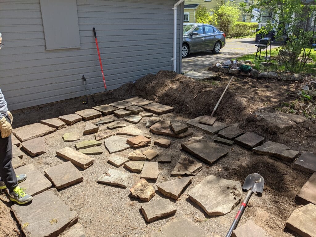 Natural stone patio taking shape in Irondequoit, with stones arranged and gaps filled with paver base.